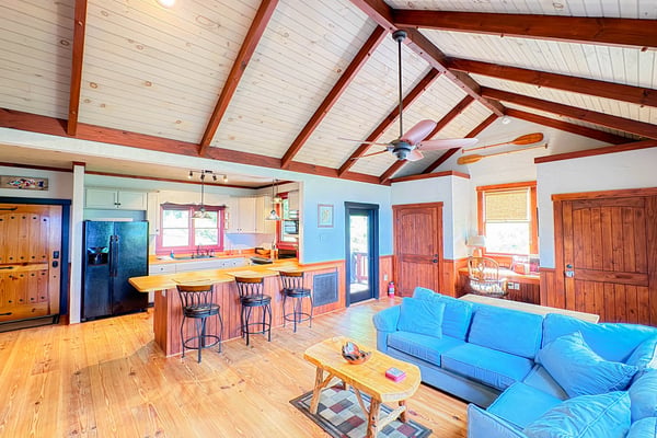 Open-plan living space with blue sofa, wooden kitchen island, exposed beam ceiling, and colorful painted walls