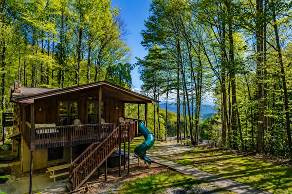 Modern cabin with deck and slide nestled among tall trees with mountain views in distance