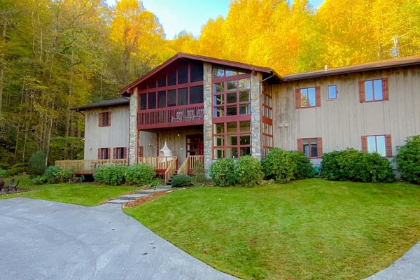 Modern house with metal siding and stone accents surrounded by golden autumn trees and manicured lawn