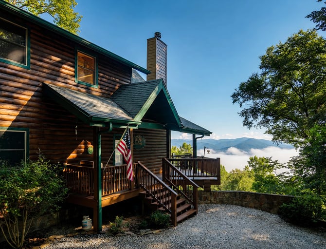 Log cabin with green trim, front porch, and American flag overlooking misty mountains and valley